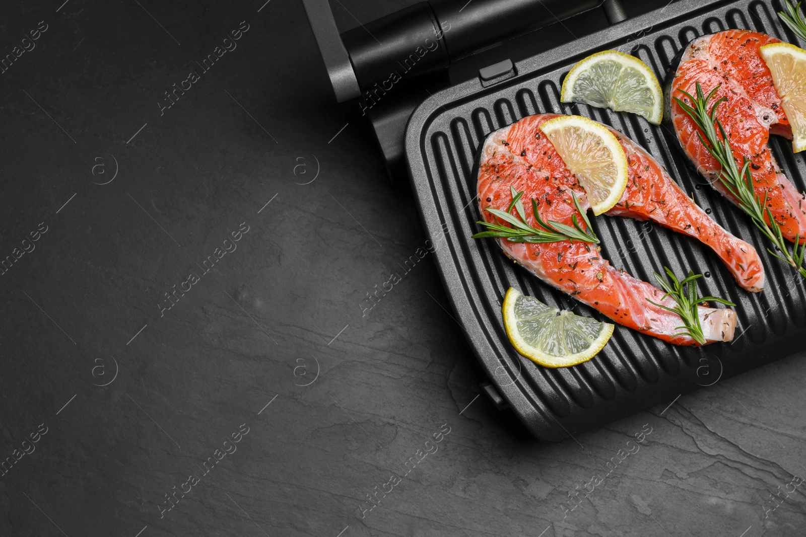 Photo of Cooking salmon. Grill with fresh fish steaks, lemon and rosemary on dark table, top view. Space for text