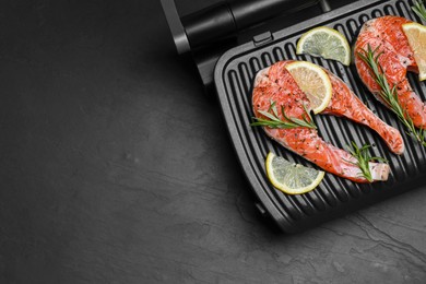 Photo of Cooking salmon. Grill with fresh fish steaks, lemon and rosemary on dark table, top view. Space for text