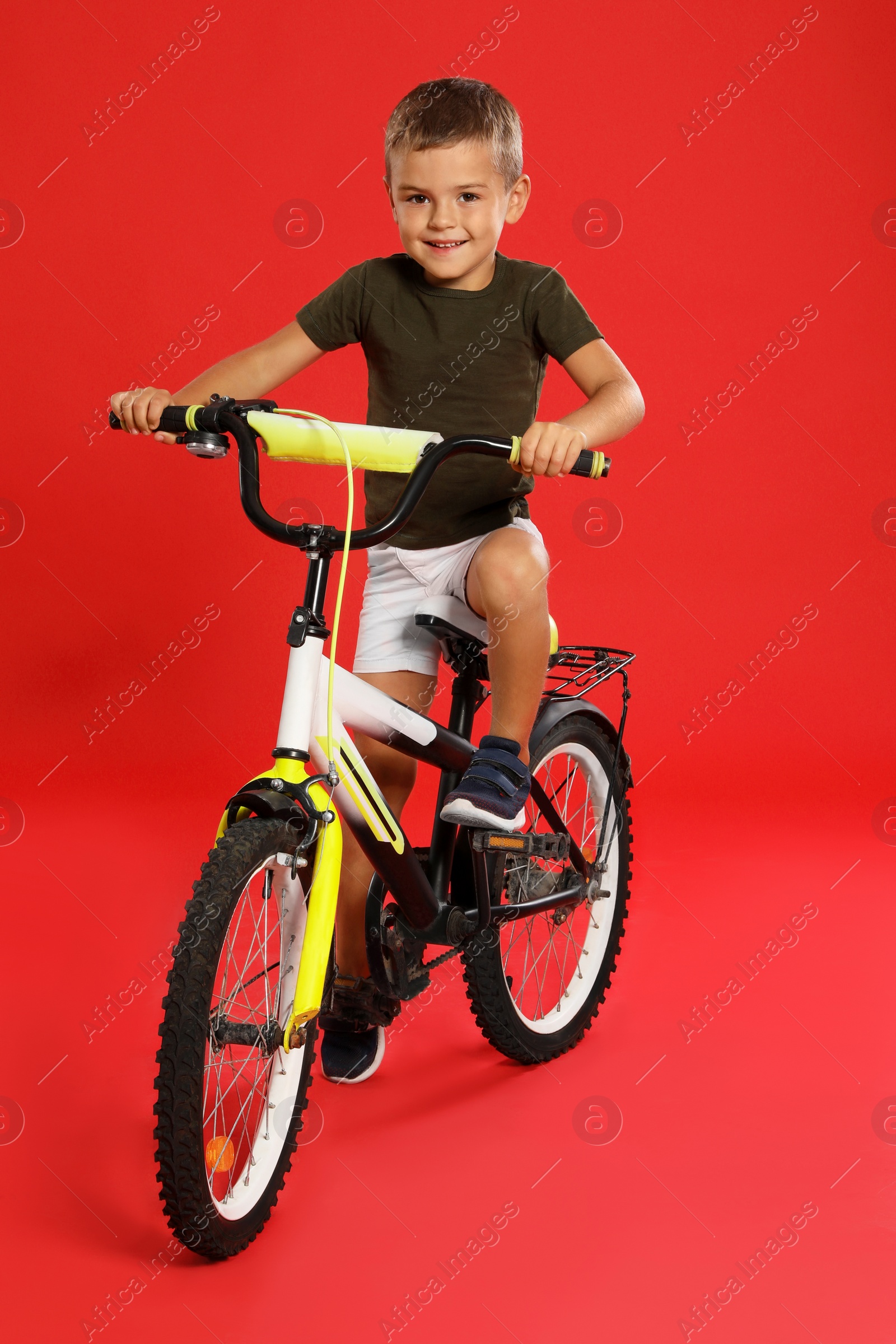 Photo of Cute little boy riding bicycle on red background