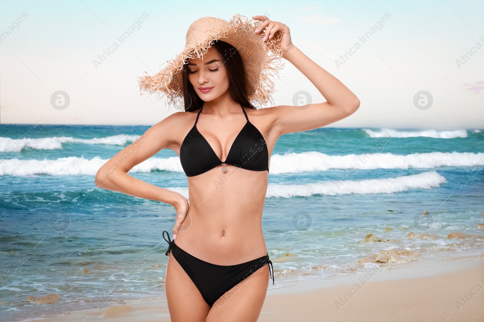 Image of Beautiful woman in stylish black bikini and hat on sandy beach near sea