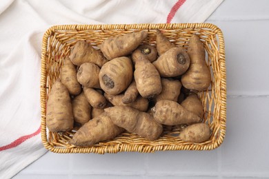 Tubers of turnip rooted chervil in wicker basket on white tiled table, top view