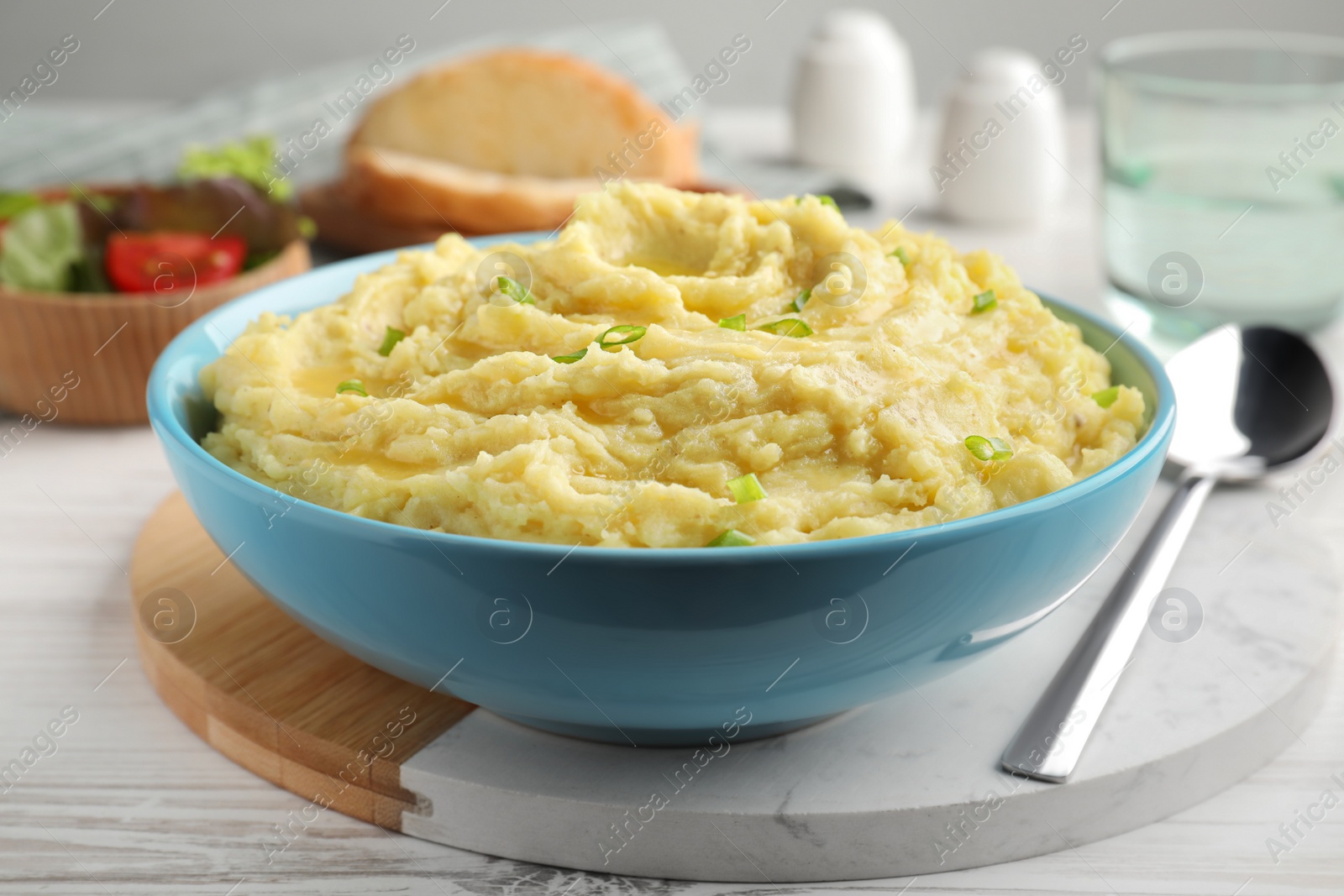 Photo of Bowl of tasty mashed potatoes with onion served on white wooden table, closeup