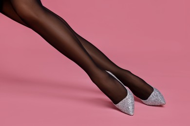 Photo of Woman with beautiful long legs wearing black tights and stylish shoes on pink background, closeup