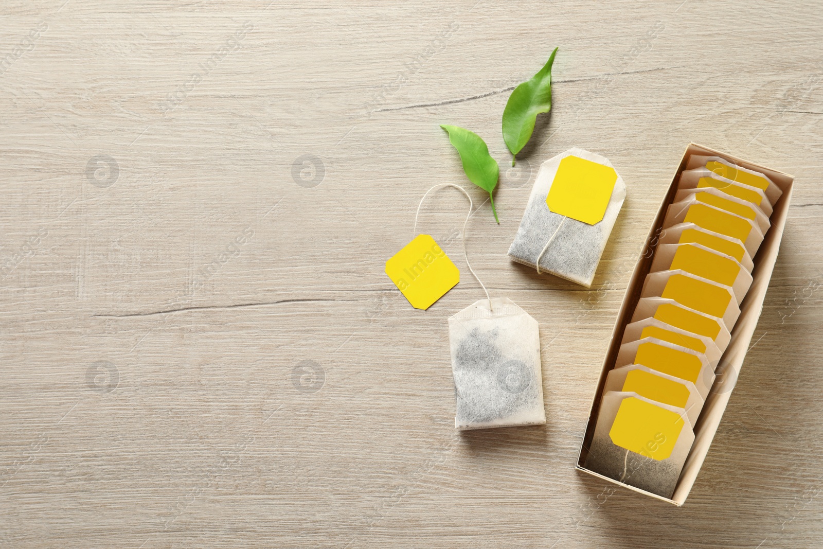 Photo of Box with paper tea bags and leaves on wooden table, flat lay. Space for text