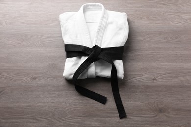 Photo of Martial arts uniform with black belt on wooden background, top view