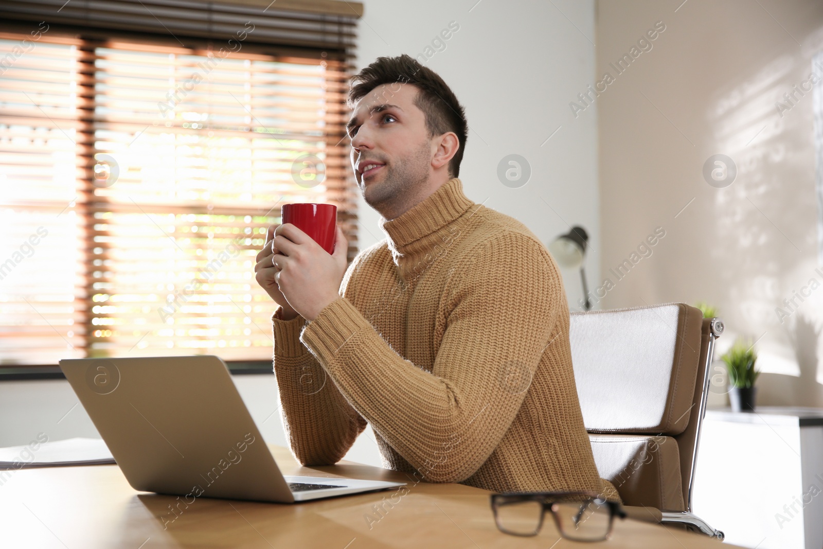 Photo of Young man with cup of drink relaxing at workplace