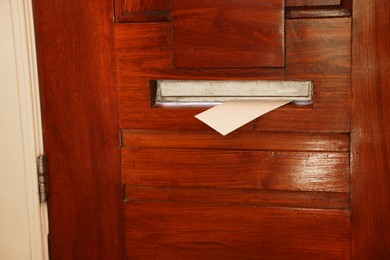 Photo of Mail slot with envelope in wooden door indoors