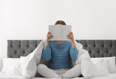 Photo of Young woman in warm sweater reading book on bed at home