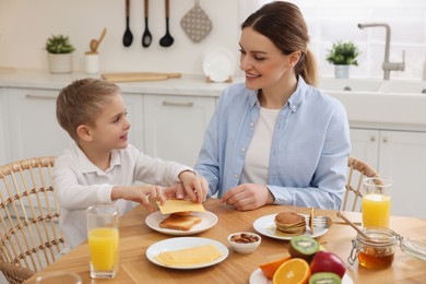 Mother and her cute little son having breakfast at table in kitchen