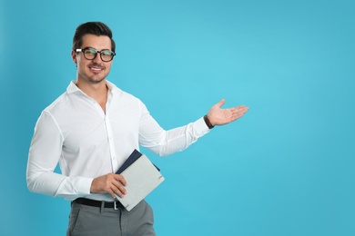 Photo of Young male teacher with glasses and notebooks on light blue background. Space for text