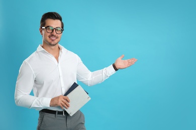 Young male teacher with glasses and notebooks on light blue background. Space for text