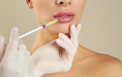Photo of Woman getting lip injection on beige background, closeup