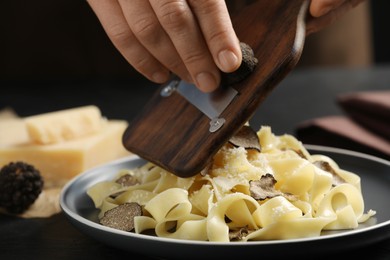 Photo of Woman slicing truffle onto tagliatelle at table, closeup