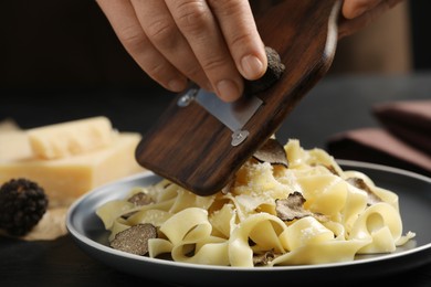 Woman slicing truffle onto tagliatelle at table, closeup