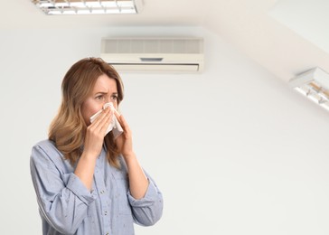 Woman suffering from cold in room with air conditioner on white wall