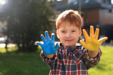 Photo of Little boy with hands painted in Ukrainian flag colors outdoors, space for text. Love Ukraine concept