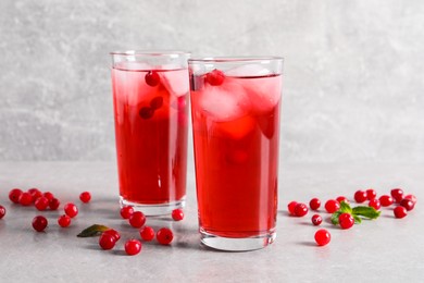 Photo of Tasty cranberry juice with ice cubes in glasses and fresh berries on light grey table
