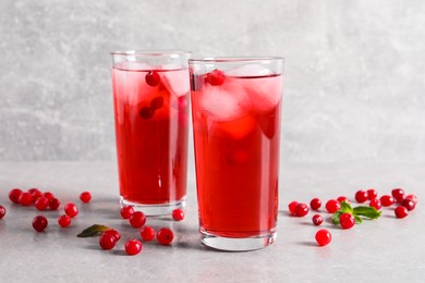 Tasty cranberry juice with ice cubes in glasses and fresh berries on light grey table