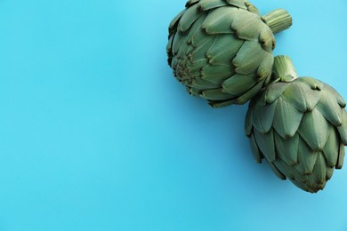 Whole fresh raw artichokes on light blue background, flat lay. Space for text