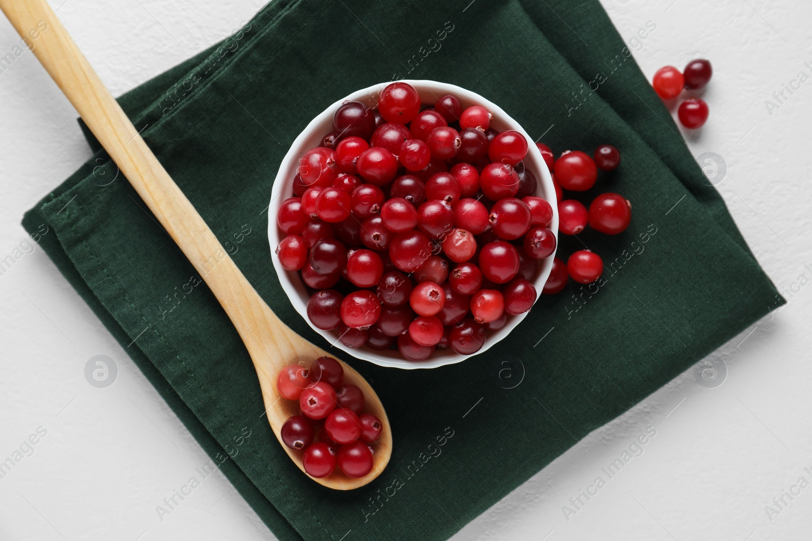 Photo of Cranberries in bowl and spoon on white table, top view