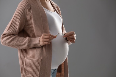 Young pregnant woman breaking cigarette on grey background, closeup. Space for text