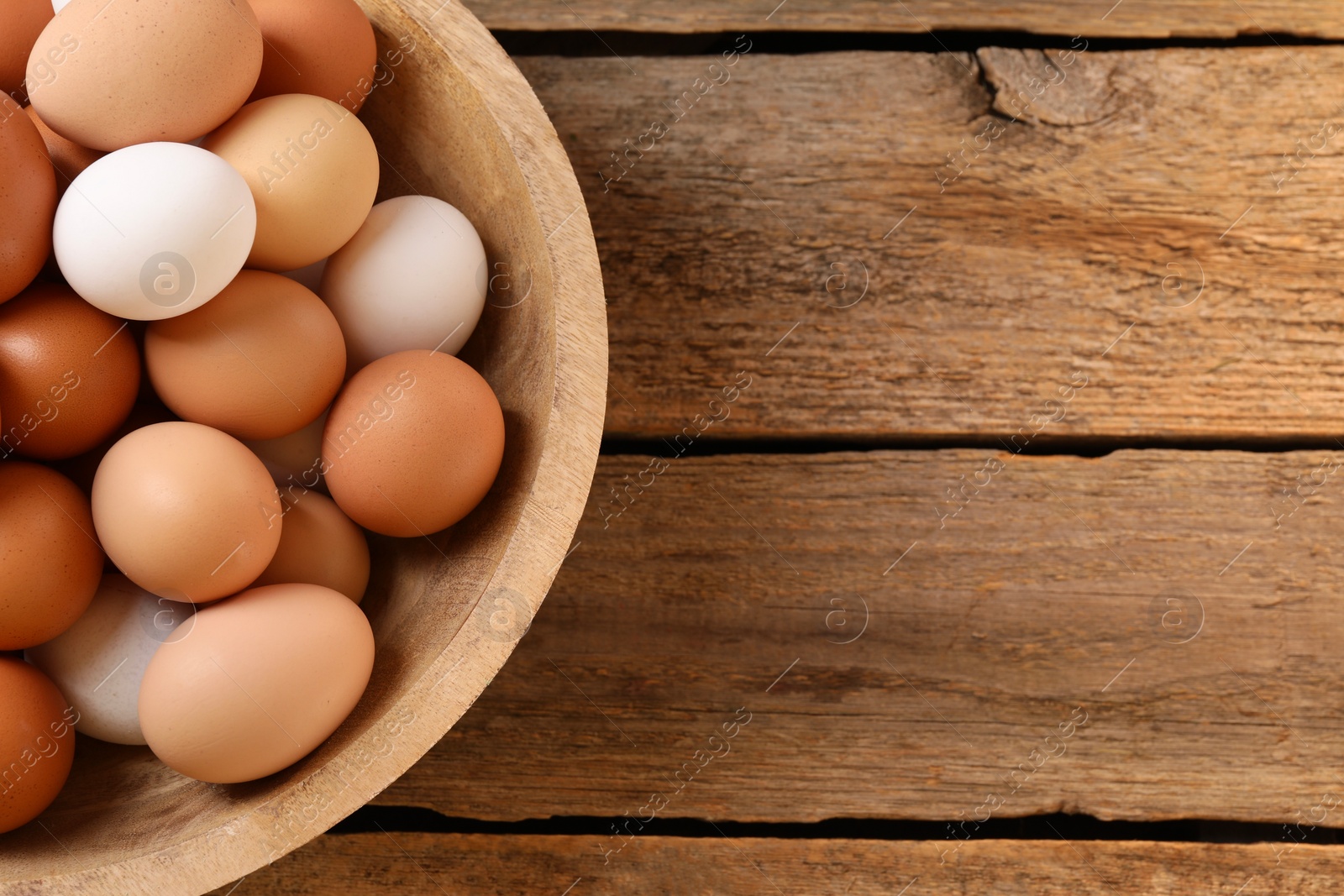 Photo of Chicken eggs in bowl on wooden table, top view. Space for text