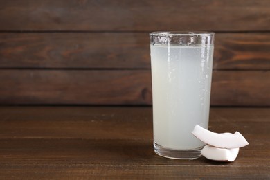 Glass of coconut water and nut on wooden table, space for text