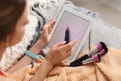 Young woman with makeup brushes using tablet on bed. Beauty blogger