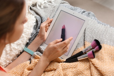 Photo of Young woman with makeup brushes using tablet on bed. Beauty blogger