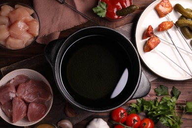 Photo of Fondue pot, forks with fried meat pieces and other products on wooden table, flat lay