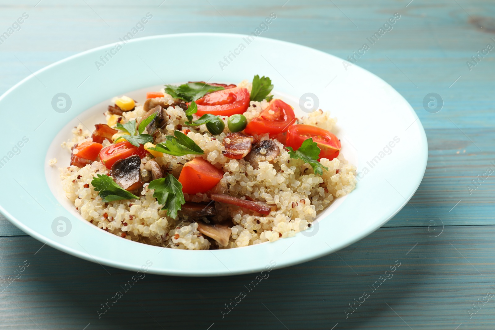 Photo of Plate of tasty quinoa porridge with fried bacon, mushrooms and vegetables on light blue wooden table, closeup