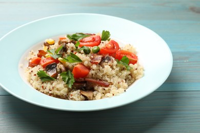 Photo of Plate of tasty quinoa porridge with fried bacon, mushrooms and vegetables on light blue wooden table, closeup