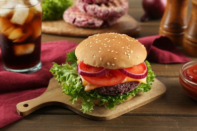 Photo of Tasty vegetarian burger with beet patty, sauce and soda drink on wooden table