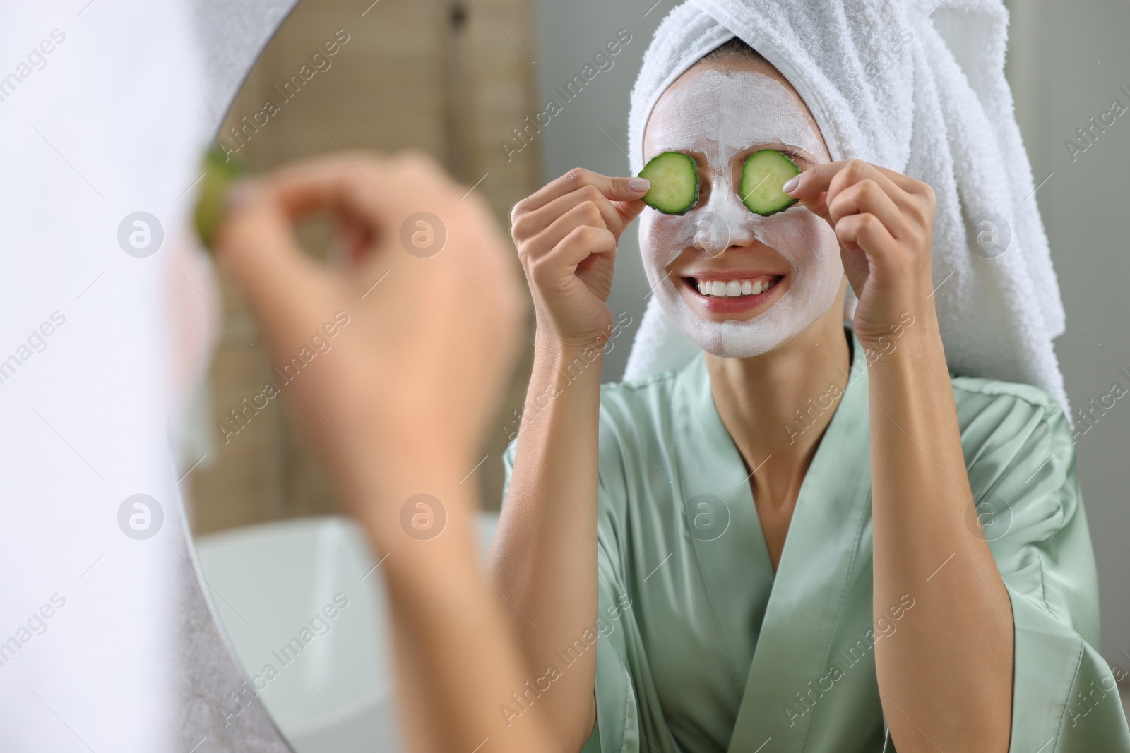 Photo of Woman with face mask and cucumber slices near mirror in bathroom. Spa treatments