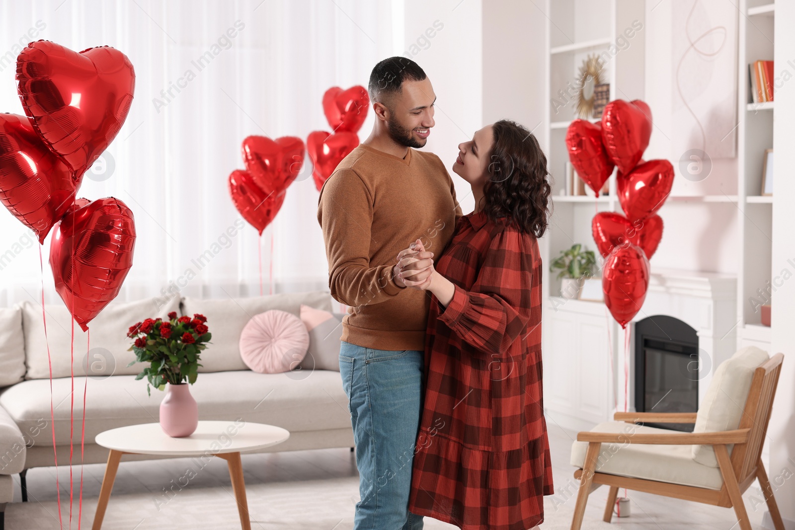 Photo of Lovely couple dancing in room decorated with heart shaped air balloons. Valentine's day celebration