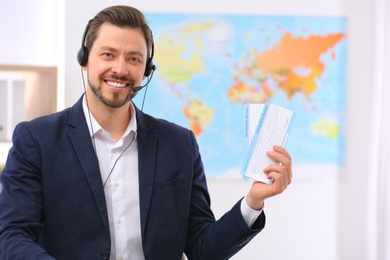 Male consultant with headset holding tickets in travel agency