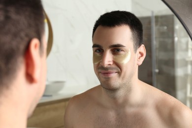 Photo of Young man with under eye patches near mirror at home