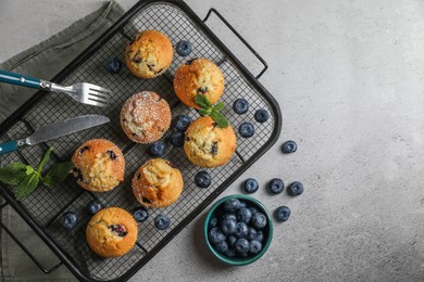 Photo of Delicious muffins with powdered sugar, blueberries and cutlery on light grey table, flat lay. Space for text