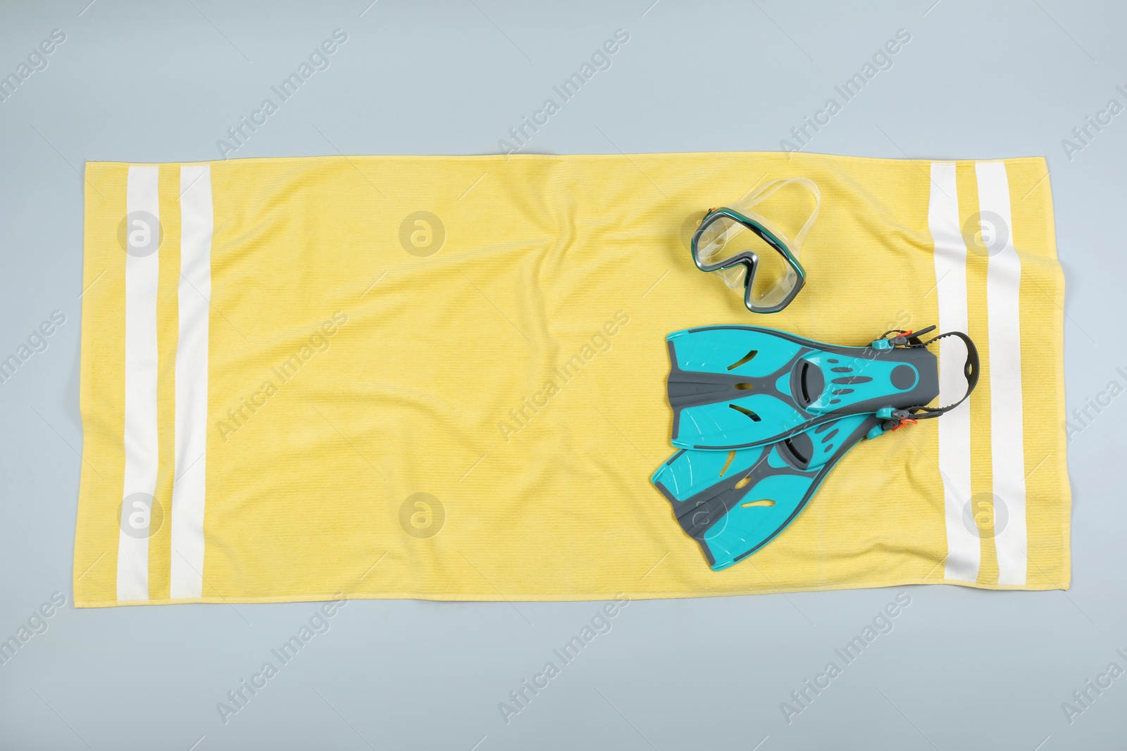 Photo of Yellow beach towel with diving equipment on light grey background, top view