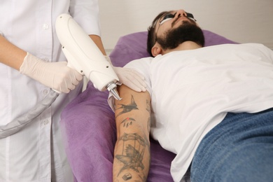 Photo of Young man undergoing laser tattoo removal procedure in salon