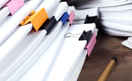 Photo of Pile of documents with colorful binder clips on wooden table, closeup