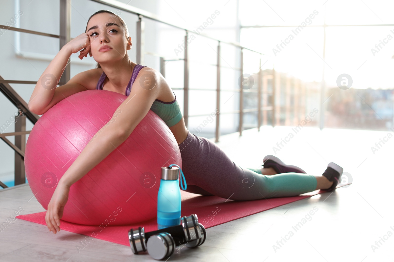 Photo of Lazy young woman with exercise ball on yoga mat indoors