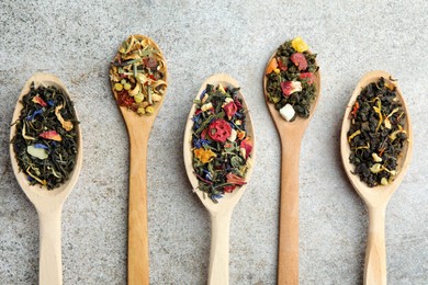 Photo of Different kinds of dry herbal tea in wooden spoons on light grey table, flat lay