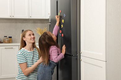 Mom and daughter putting magnetic letters on fridge at home. Learning alphabet