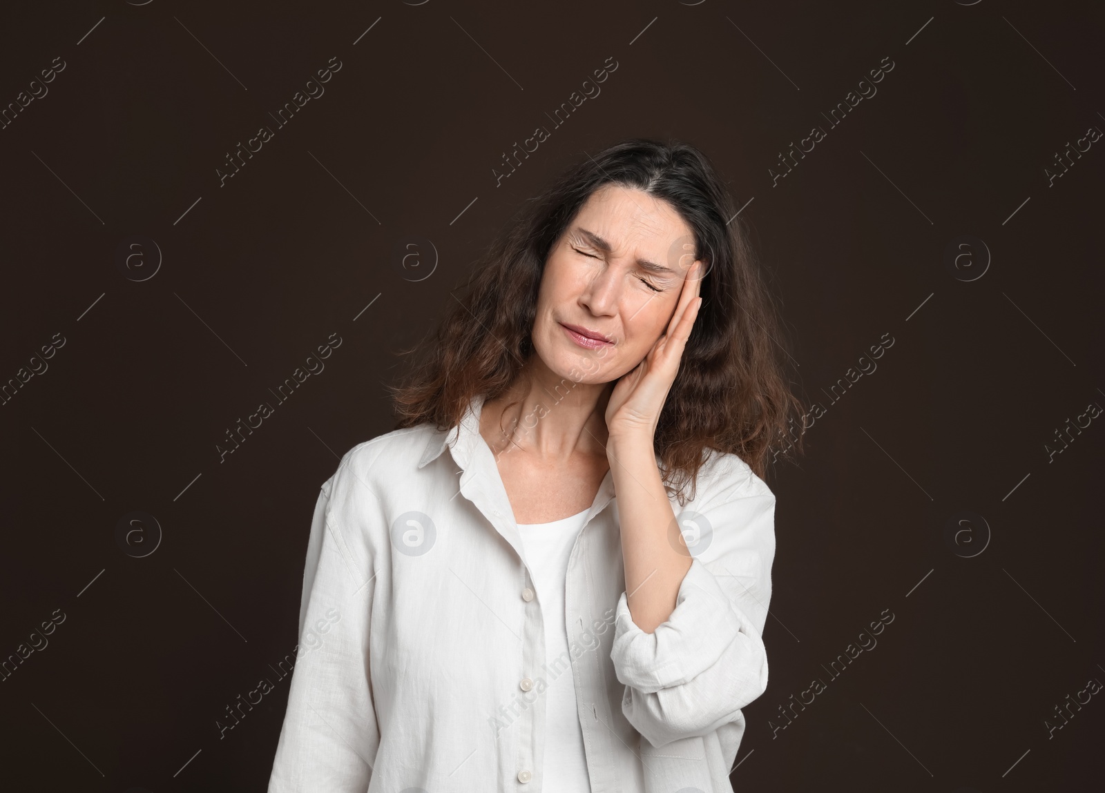 Photo of Mature woman suffering from headache on dark brown background