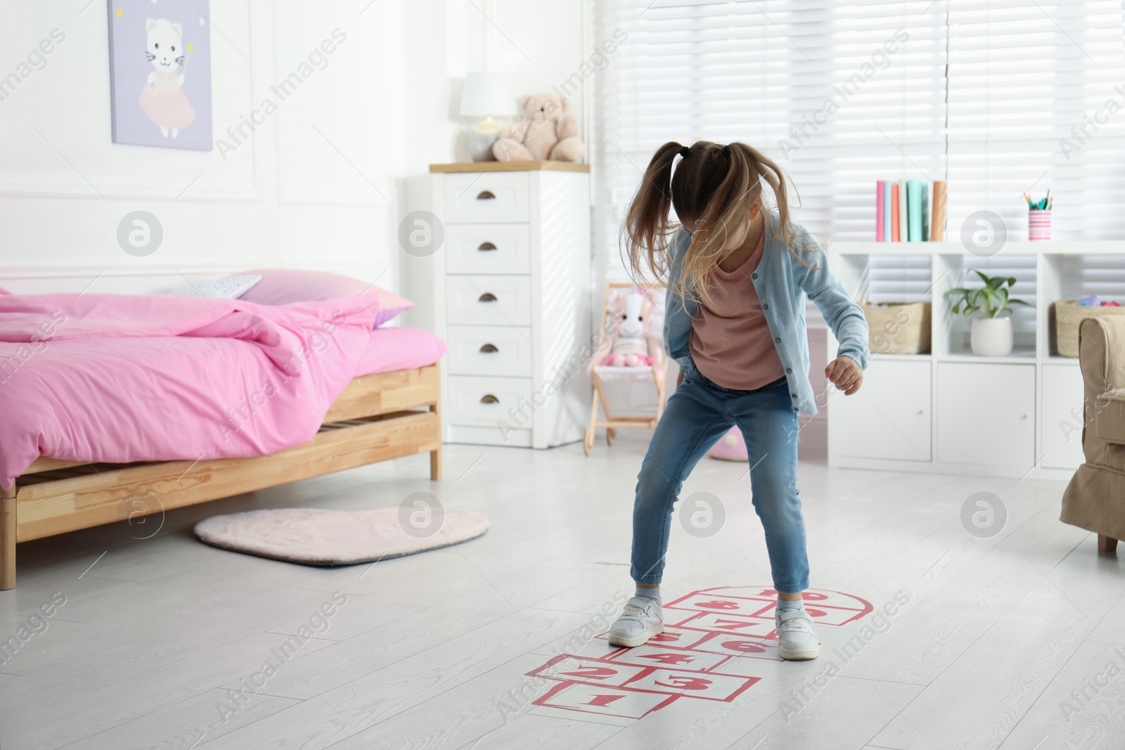 Photo of Cute little girl playing hopscotch at home