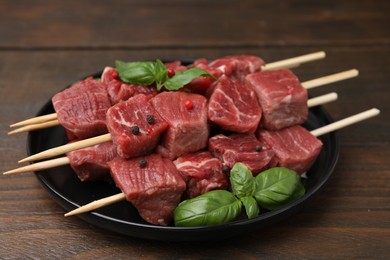 Skewers with cut fresh beef meat, basil leaves and spices on wooden table