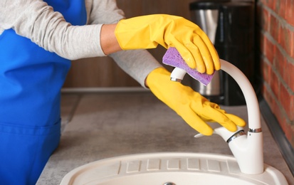 Photo of Woman cleaning tap with sponge in kitchen, closeup