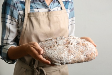 Photo of Woman holding freshly baked bread on grey background, closeup