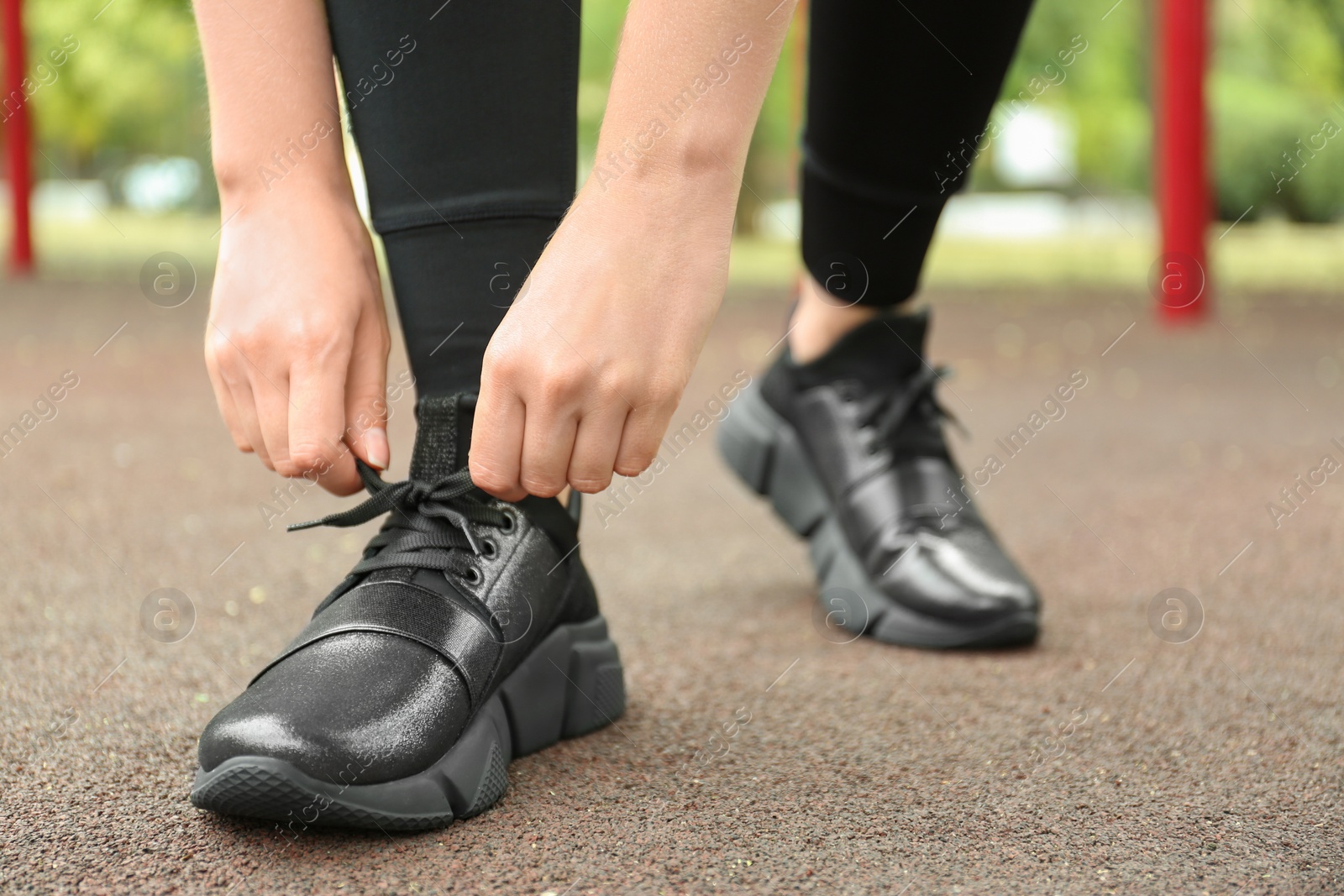 Photo of Woman tying laces of stylish sneakers outdoors, closeup